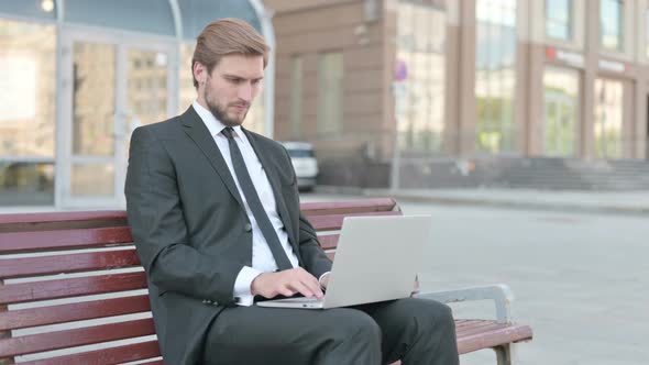 Businessman with Laptop Smiling at Camera While Sitting Outdoor on Bench