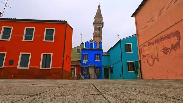 Low angle ground surface fpv pov toward colorful houses and leaning belltower of Burano in Italy. Sl