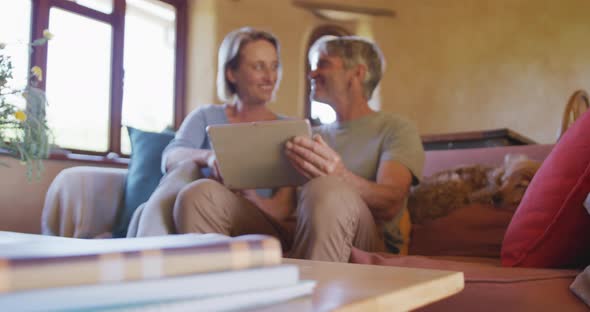 Smiling senior caucasian couple using tablet and sitting in living room