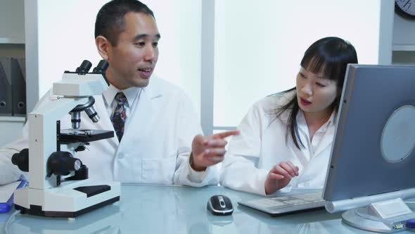 Scientists in lab work with microscope and computer