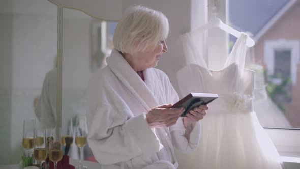 Happy Senior Woman Looking at Photo in Frame and Looking Back at Wedding Dress