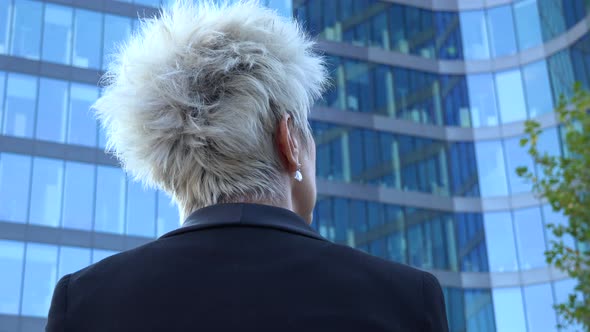 A Middle-aged Businesswoman Looks at a Windowed Office Building - Closeup From Below