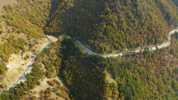 Empty winding mountain road through autumn forest, aerial side shot