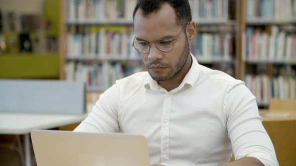 Thoughtful Young Man Typing on Laptop in Library