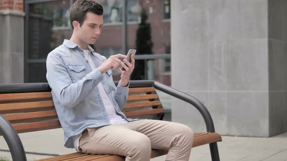 Casual Young Man Using Smartphone Sitting Outdoor