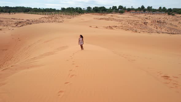 aerial tracking backwards of woman walking top of desert sand dunes in Mui Ne Vietnam