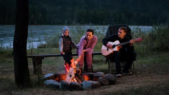 Family of Three Enjoying Vacation By the Campfire