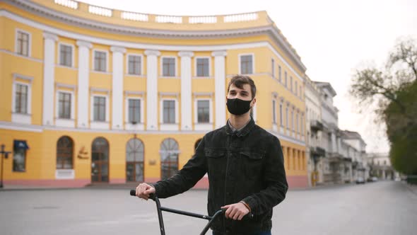 Young Guy in Protective Face Mask Walking with His Bike in the Street of Empty City Center Slow