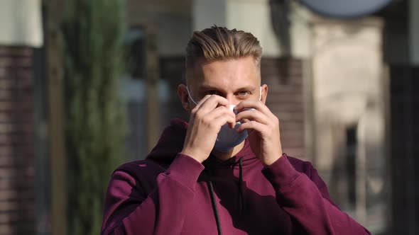 Portrait of a Young Man Looking at the Camera and Putting on a Medical Mask To Protect His Face From