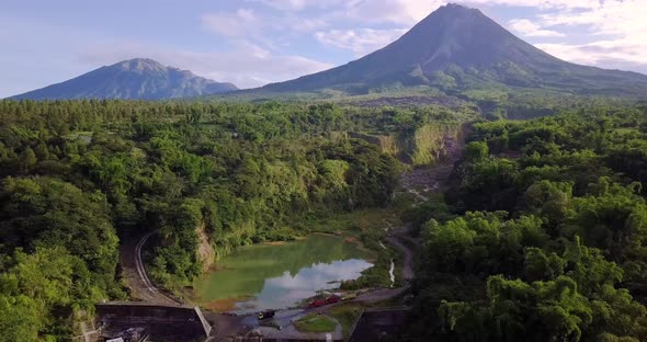 Aerial backwards flight showing natural lake surrounded by wilderness of Indonesia and giant Merapi