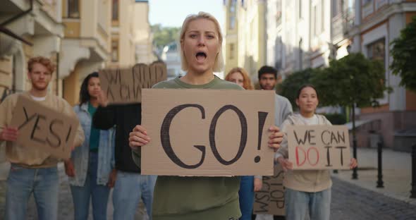 Blond Woman in Front Shows Go Poster to Protest Against Racism with Activists Protesting Students