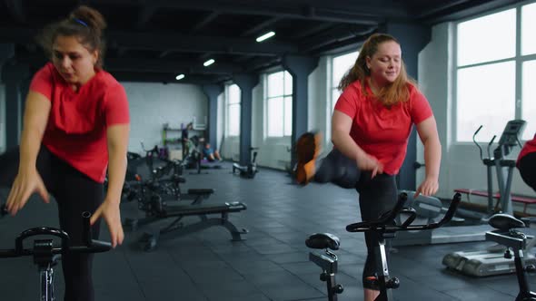 Group Athletic Girls Performing Aerobic Riding Training Exercises on Cycling Stationary Bike in Gym