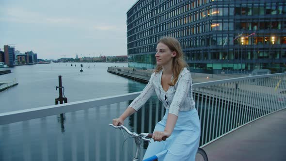 Young Blond Woman Riding Bicycle Along Bridge