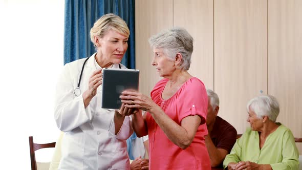 Female doctor assisting senior woman on digital tablet