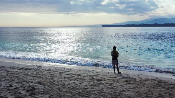 Man fishing alone on paradise lagoon beach voyage by shallow sea and white sandy background of Lombo