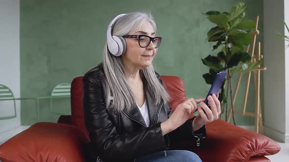 Modern 60-Aged Woman with Long Gray Hair which Wearing Glasses and Enjoying Nice Music on Headphones