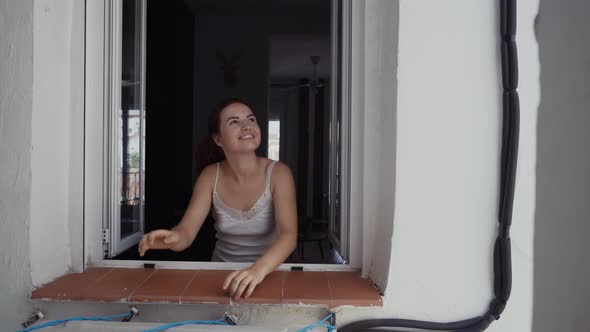 Young woman standing near window and looking outside