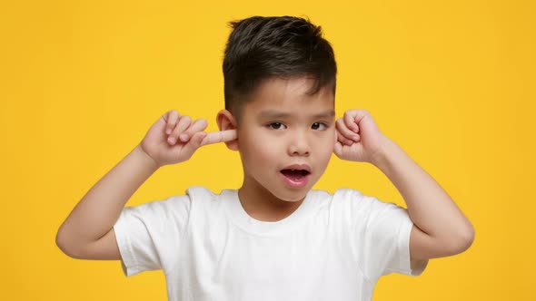 Naughty Asian Little Boy Covering Ears Shaking Head Yellow Background