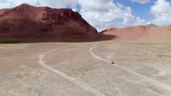 Aerial View of a Car Driving in a Curved Dirt Road in the Tajikistan Desert