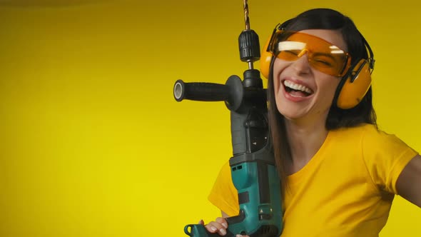 A Cheerful Woman in Protective Headphones is Holding a Drill in Her Hand