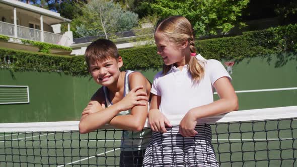 Portrait of caucasian brother and sister smiling together while standing at at tennis court on