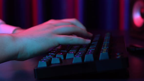 A Young Man Is Typing on a Computer Keyboard. Hands Close Up. Blue and Red Light Falls on the Hands.