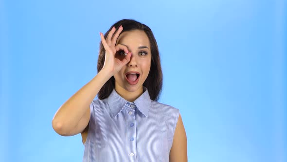 Young Woman Making OK Gesture Looking Through Fingers and Winking