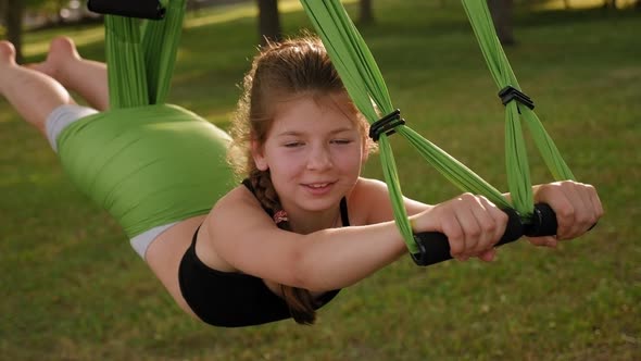 A Little Girl Practices Yoga on a Hammock in a Park in a Tree. Anti-gravity Yoga