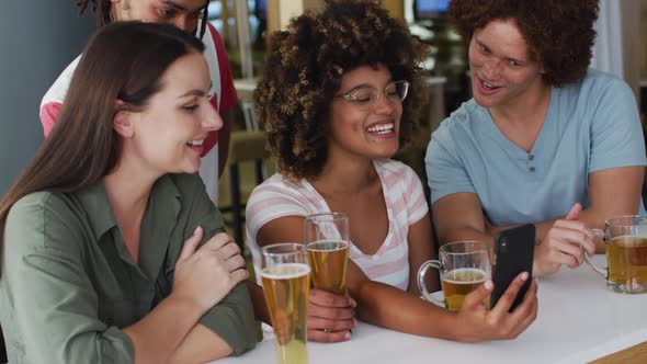 Diverse group of happy friends drinking beers and using smartphone at a bar