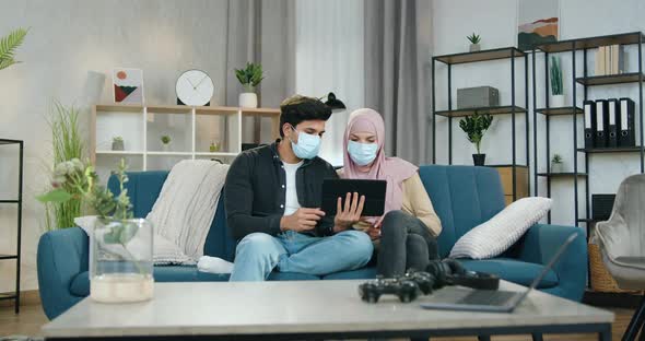 Arabic Couple in Medical Masks Sitting Together at Home and Uses Tablet Device to Read News
