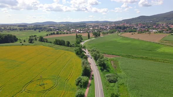 Aerial View of Cars Moving on Road Through Agricultural Fields Near Mountains