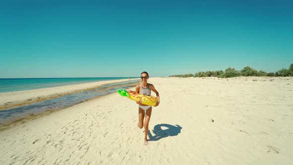 Cheerful Happy Young Attractive Woman Runs on Empty Sunny Sandy Beach Holding Yellow Inflatable