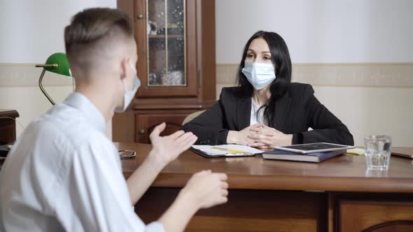 Supportive Caucasian Woman in Covid Face Mask Listening To Stressed Man Talking Sitting