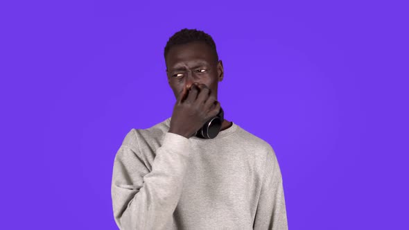 Afro American Man Isolated Against Blue Background with Headphones on Neck Smelling Something Stinky