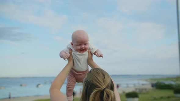 Mother Holding Up Baby Girl At Seaside