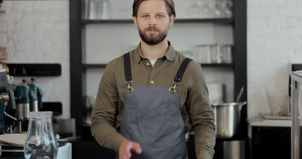 Handsome Man Barista Standing at Counter in Bar Looking at Camera and Crossing Hands