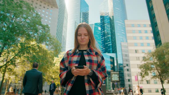 Young Woman Uses Smartphone App Walking in Paris Downtown with Skyscrapers