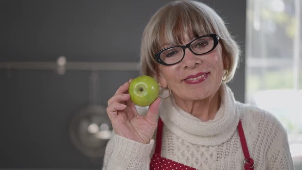 Portrait of Smiling Senior Woman Posing with Vitamin Healthful Green Apple Indoors