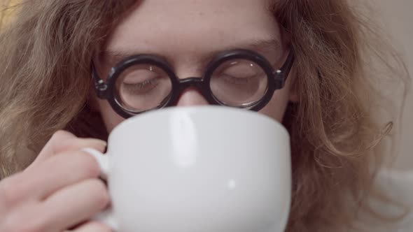 Closeup Face of Nerd Young Man in Retro Eyeglasses Drinking Tea or Coffee Looking at Camera and