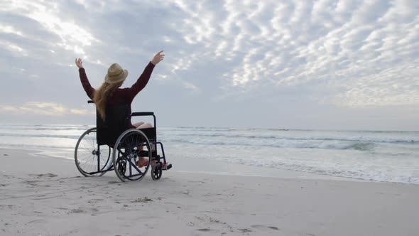 Rear view of young disabled caucasian woman in hat sitting on wheelchair and arms outstretched 4k