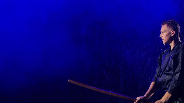 Side View of Japanese Kendo Fighter Practicing Martial Skill Under Rain on Dark Studio Background