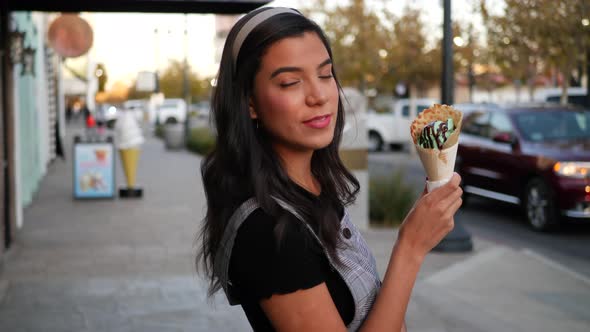 A cute young hispanic woman holding an ice cream cone and smiling with happiness at a dessert shop o