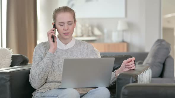 Cheerful Woman with Laptop Talking on Smartphone at Home 