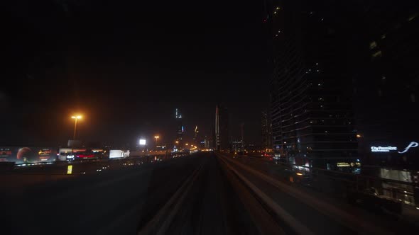 Dubai Metro Train Driving Past Skyscrapers in Urban City Center at Night