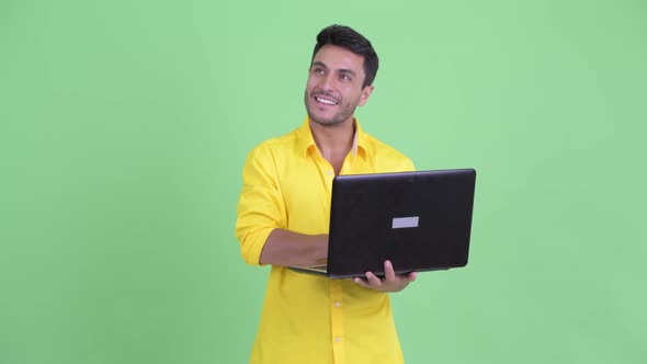 Happy Young Hispanic Businessman Thinking While Using Laptop