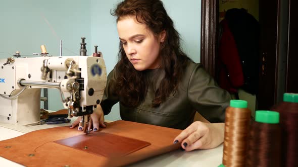 Brunette Seamstress Sews a Pocket To a Leather Bag in a Sewing Workshop. A Woman Operates Sewing