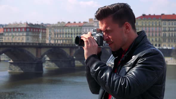 A Young Handsome Man Takes Photos with a Camera - Closeup - a River and a Quaint Town