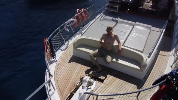 Male Caucasian Topless Tourist Resting on the Deck of Yacht and Using Smartphone in His Hand