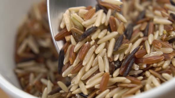 Mixed various types of Asian long basmati rice. Scooping with a metal spoon from a white bowl