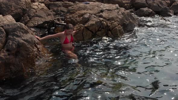 Lady in Red Bikini Climbs Down Into Water From Stone Beach